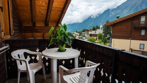 A wooden balcony with a table and chairs, overlooking a mountainous landscape with a church tower. - Hotel Santa San (Ayas)