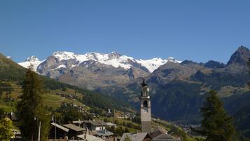 A mountain village with a prominent church tower, surrounded by snow-capped peaks and lush greenery.