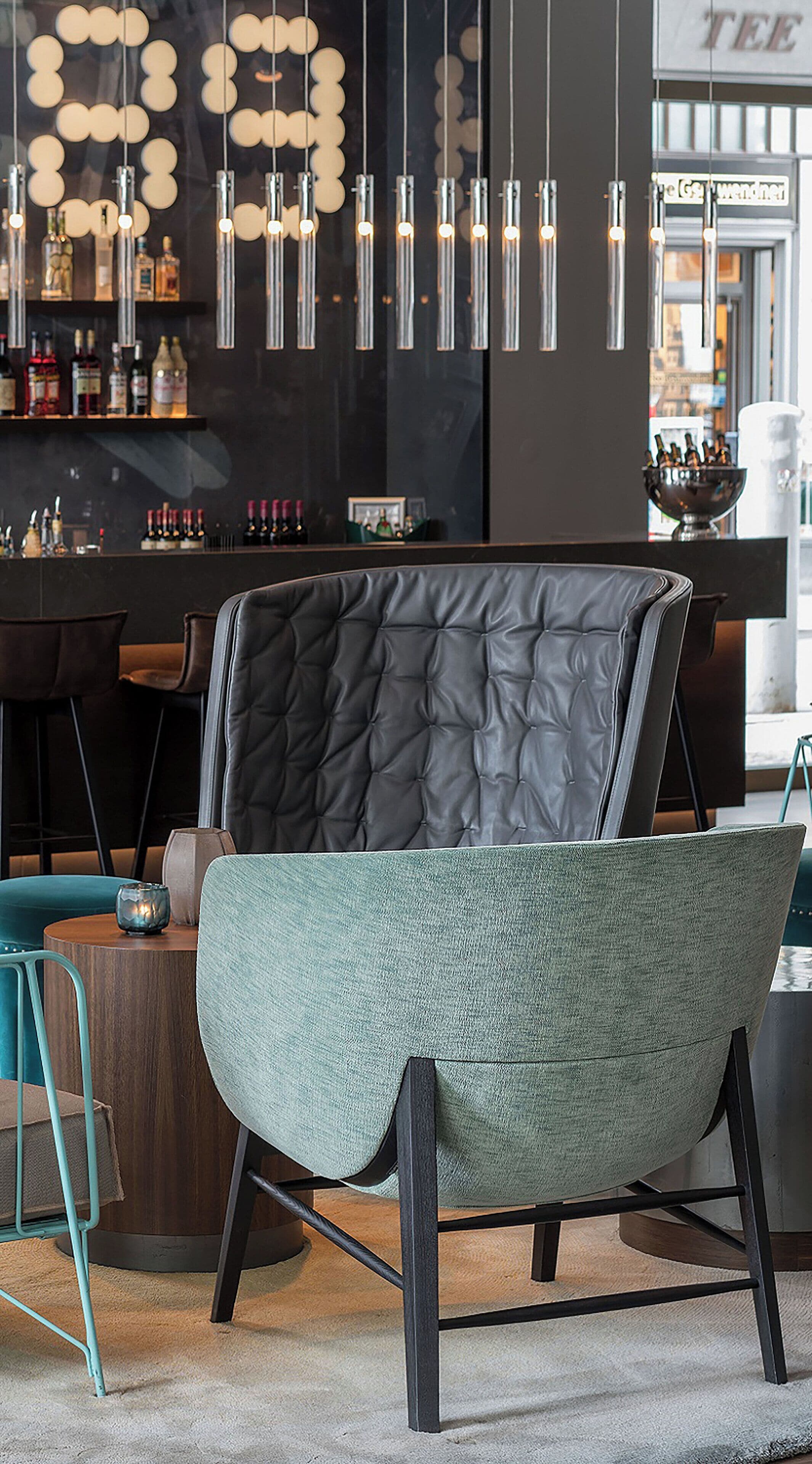 A modern bar area with a tufted leather chair, a bar counter with bottles, and pendant lighting.