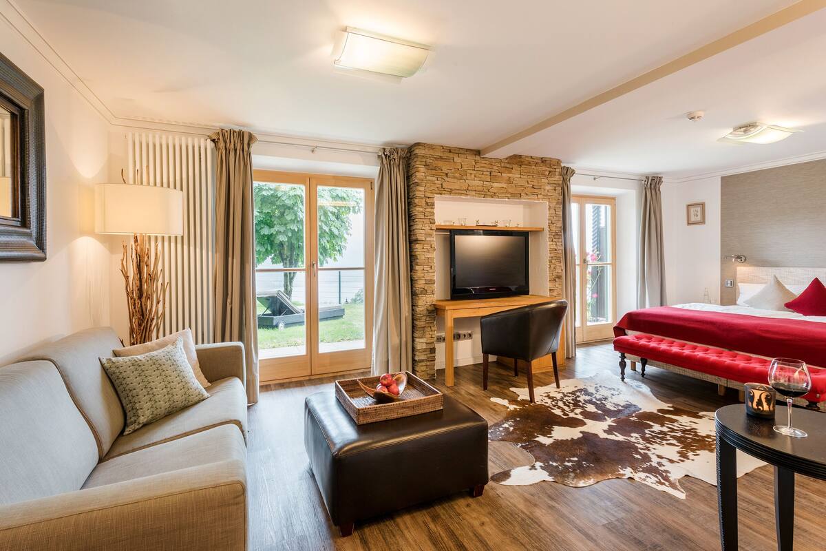 Un salon moderne avec un canapé, un pouf, un téléviseur et un lit rouge.