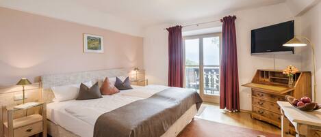 A hotel room with a bed, bedside tables, a desk with a chair, a TV, and a window with curtains.