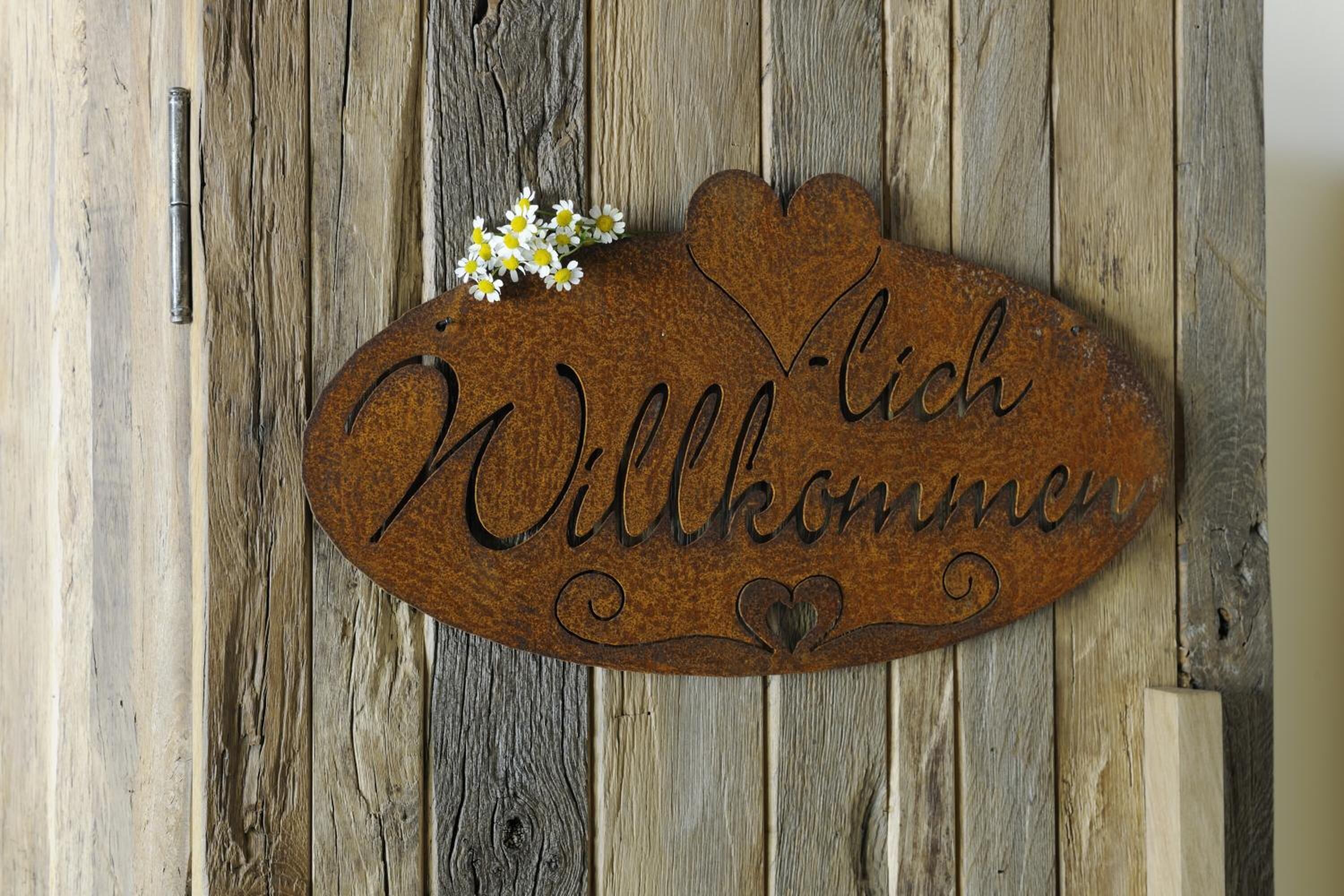 A wooden welcome sign with the text "Willkommen" on a rustic wooden background.