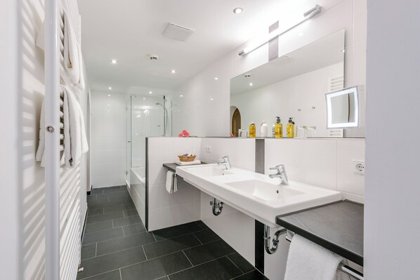 A modern bathroom with a dual sink, a large mirror, and a shower area. - Der Westerhof Tegernsee Hotel (Tegernsee)