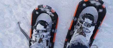 Un par de botas de esquí cubiertas de nieve, con detalles naranja y un marco negro, sobre una superficie nevada.