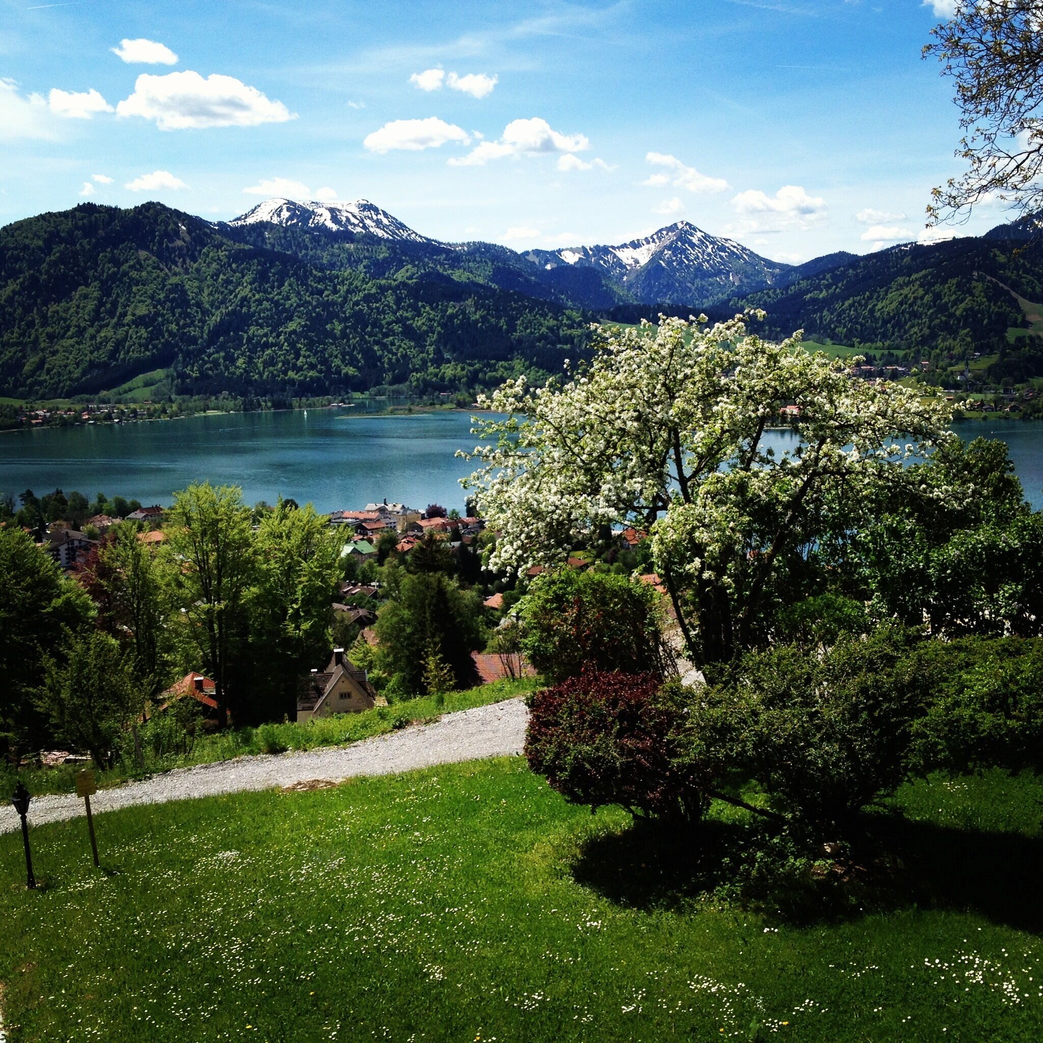Vista panorámica de un lago rodeado de montañas y vegetación, con un sendero que lleva a un edificio.
