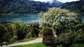 Vista panorámica de un lago rodeado de montañas y vegetación, con un sendero que lleva a un edificio.