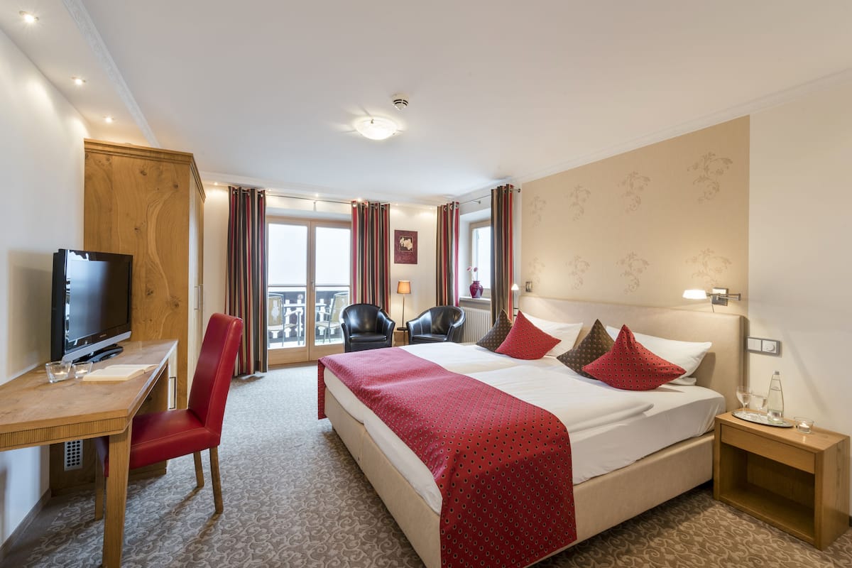 Une chambre d’hôtel avec un lit, un bureau avec une télévision, une chaise et une fenêtre avec des rideaux.