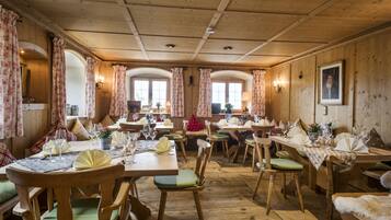 A wooden interior with multiple dining tables and chairs, each set with tableware and glassware.
