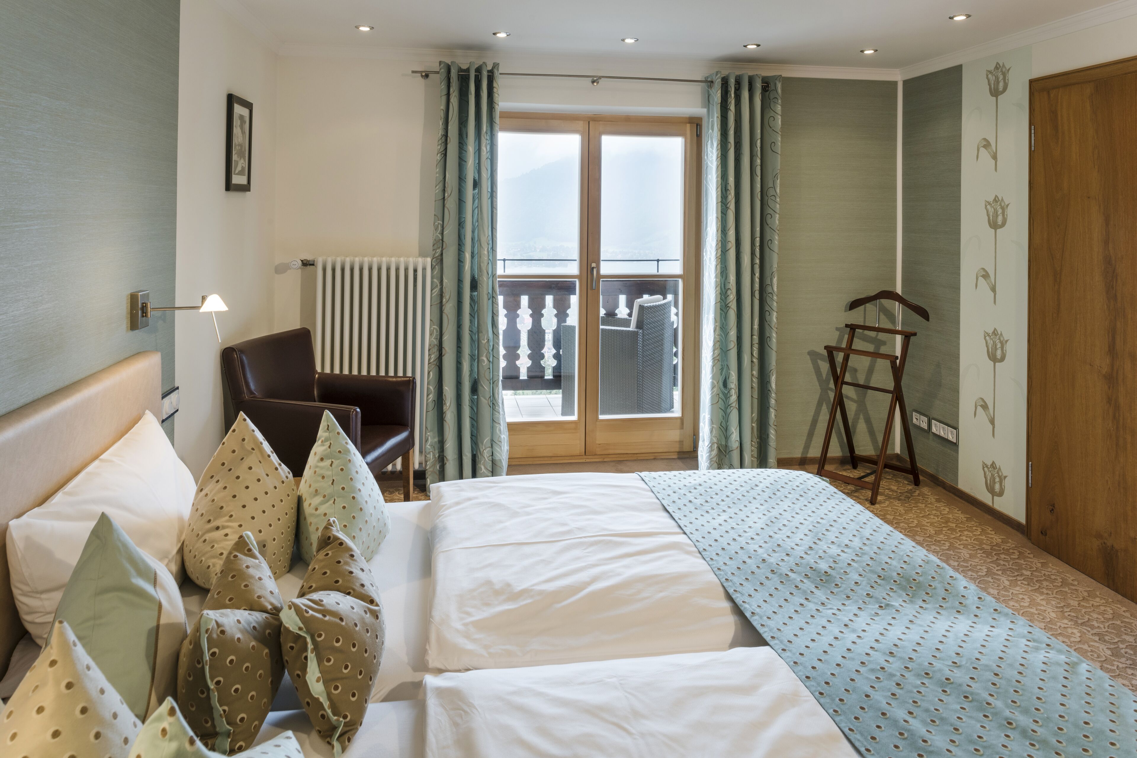Una camera d'albergo con un letto, una sedia, un termosifone, una porta e vista sull'esterno.