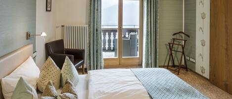 Una camera d'albergo con un letto, una sedia, un termosifone, una porta e vista sull'esterno.