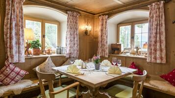 A wooden dining room with a table set for four, flanked by two windows with curtains.
