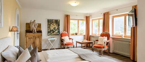 Une chambre d’hôtel avec un grand lit, deux fauteuils, une petite table, une armoire en bois et un tableau au mur.