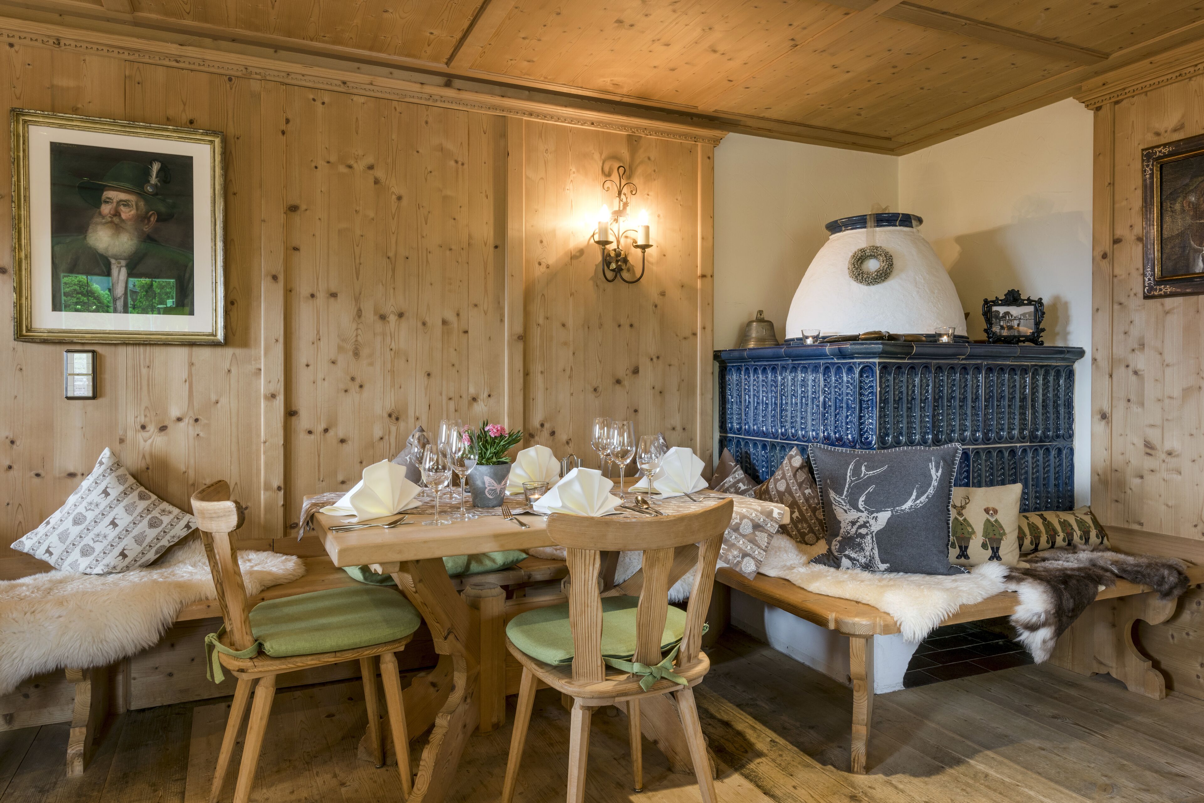 A wooden interior with a dining table set for four, a sofa with patterned cushions, and a decorative fireplace.