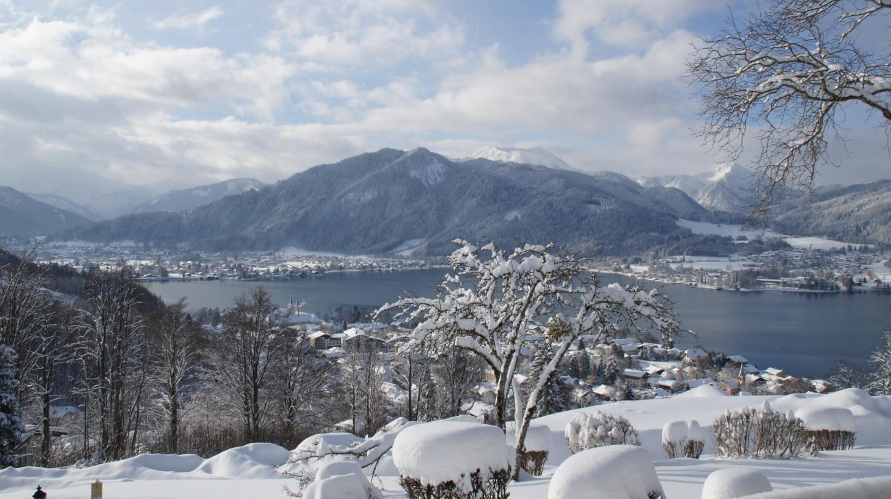 A snow-covered landscape with mountains, a lake, and a town in the background.
