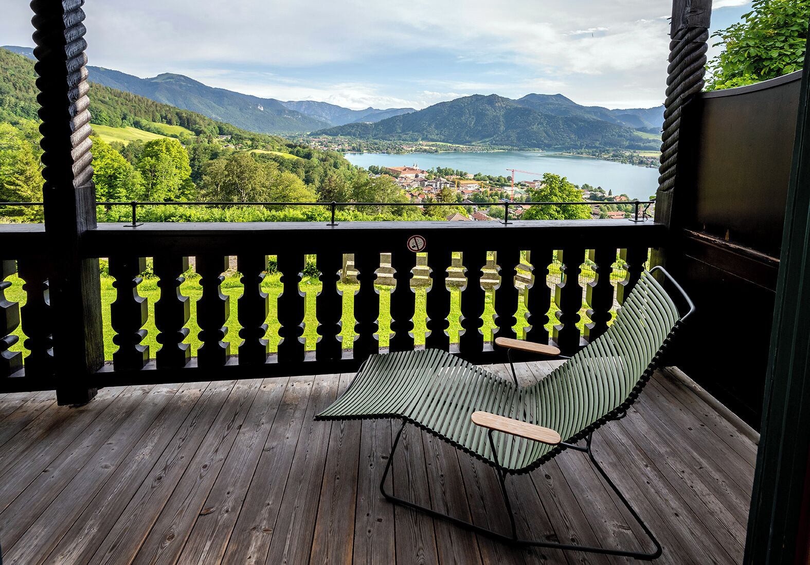Una terraza de madera con barandilla de metal negro y una silla hamaca verde.