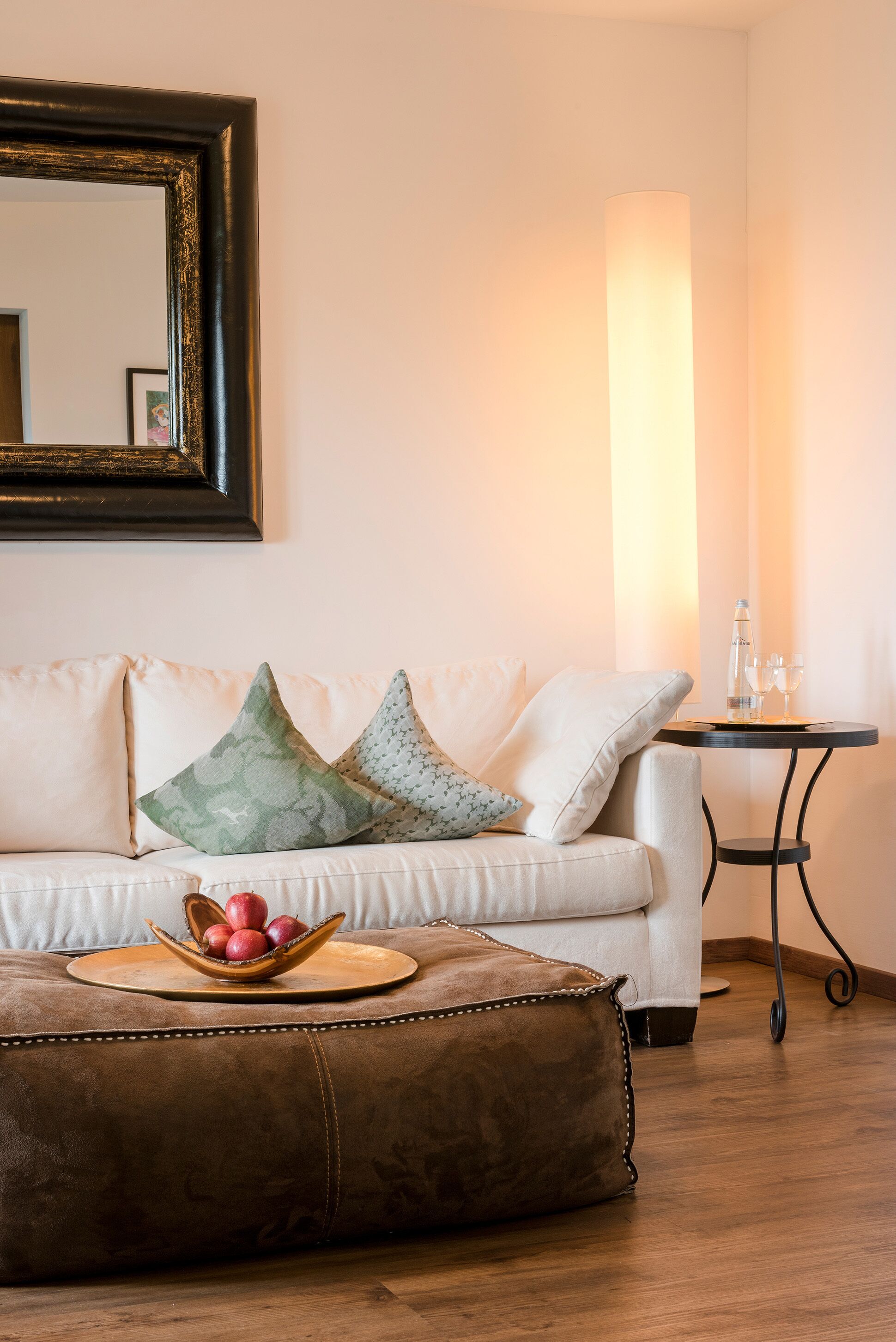 En vit soffa med en läderklädd pall, ett litet bord med en vattenflaska och glas, och en hög golvlampa.