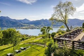 A lakeside view with a dining area overlooking the water and mountains. - Der Westerhof Tegernsee Hotel (Tegernsee)