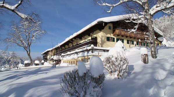 Un edificio cubierto de nieve con un balcón de madera y árboles nevados.