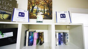 Una estantería con libros y dos carteles de valoración de huéspedes para Flexistay Aparthotel, uno correspondiente a 2012 y otro a 2013, ambos con una puntuación de 8,1.