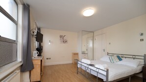 Un dormitorio con una cama, una mesita de noche, un televisor, una ventana y un espejo.