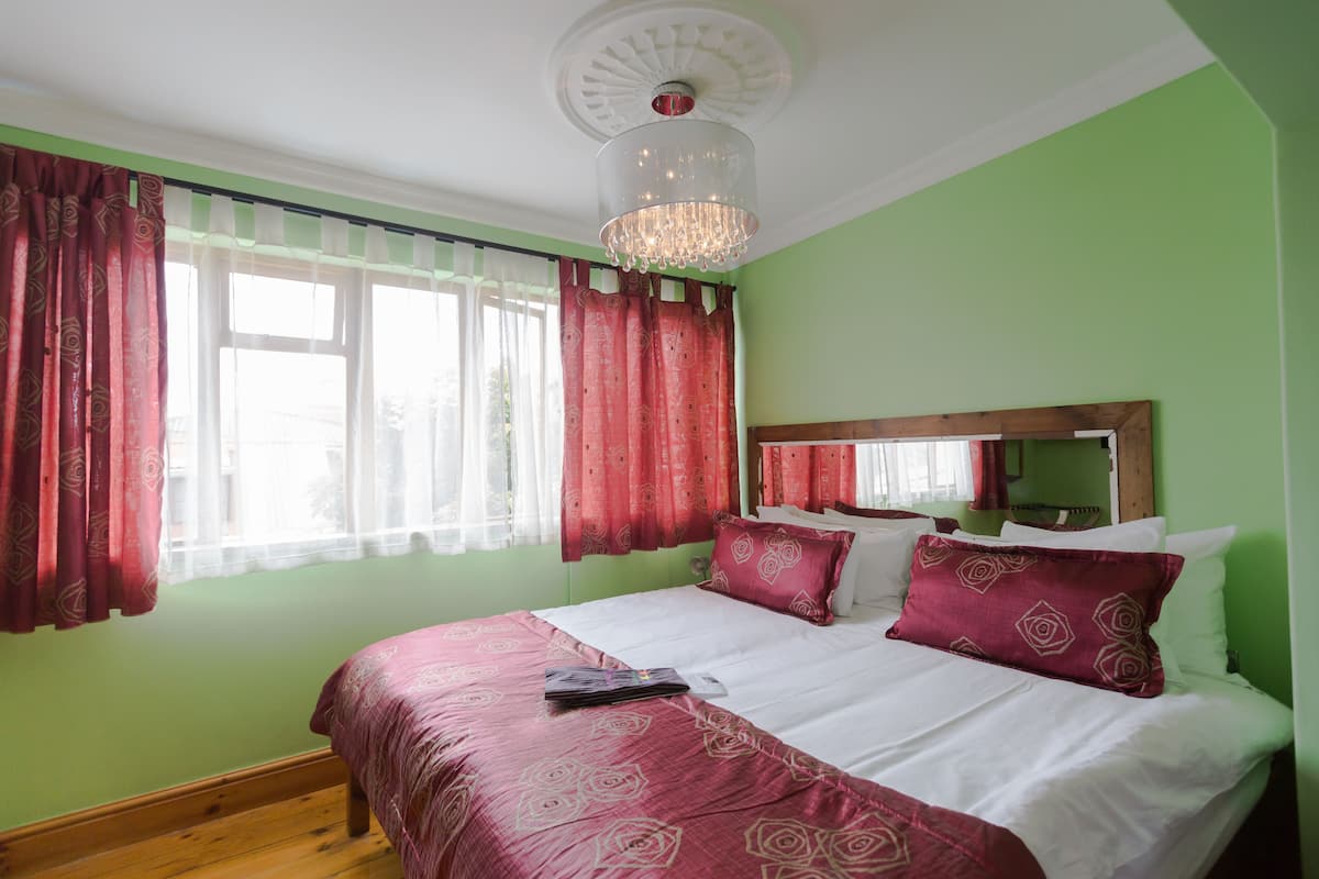 Un dormitorio con cama, cortinas, una araña y una pared verde.