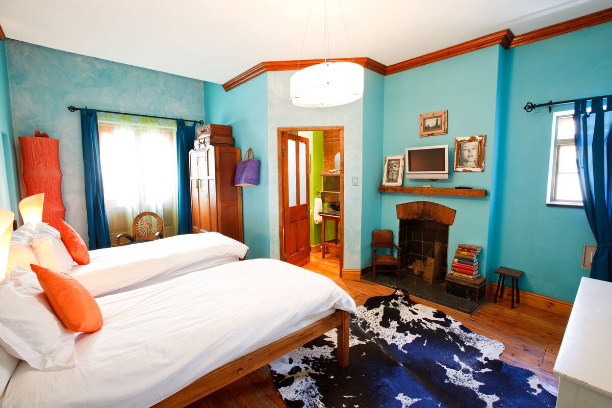Un dormitorio con dos camas, una chimenea y vistas a una habitación verde a través de una puerta abierta.
