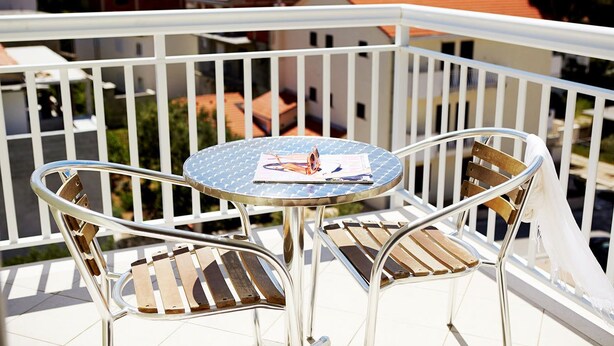 A balcony with a round table and two chairs, overlooking a residential area with red-roofed houses. - Apartments Ivana (Baska Voda)