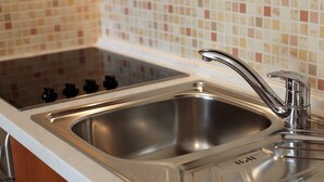 A kitchen with a stainless steel sink, a faucet, and a stove with four burners. - Apartments Ivana (Baska Voda)