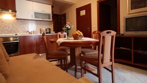 A cozy kitchen with wooden cabinets, a dining table with chairs, a sofa, and a television. - Apartments Ivana (Baska Voda)