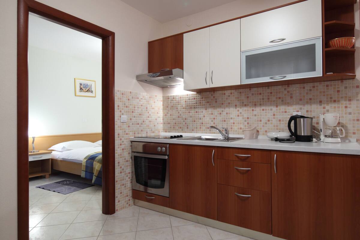 A compact kitchen with wooden cabinets, a microwave, an oven, and a sink.