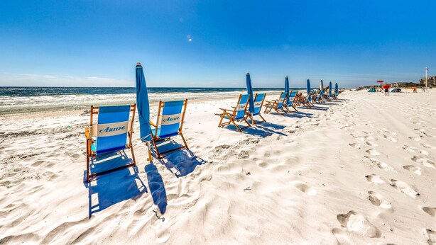 A beach with rows of blue beach chairs and umbrellas, a sandy shore, and the ocean in the background. - Azure Condominiums (Fort Walton Beach)