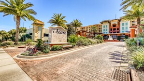 A hotel entrance with a sign reading "Azure," paved walkway, palm trees, and buildings in the background. - Azure Condominiums (Fort Walton Beach)