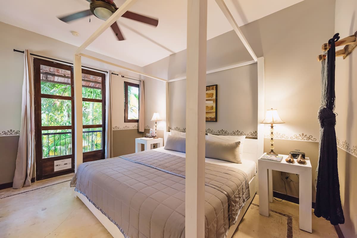 A bedroom with a bed, two bedside tables with lamps, a ceiling fan, and a window with curtains.