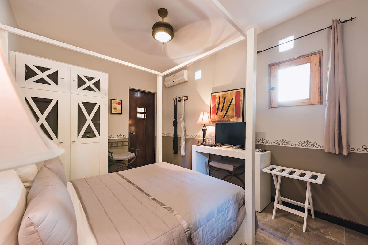 A bedroom with a bed, a desk, a chair, a TV, and a window.