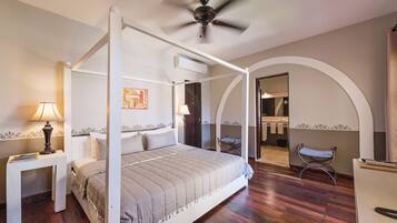 Ein Himmelbett mit Deckenventilator, ein Nachttisch mit Lampe und ein Holzboden.
