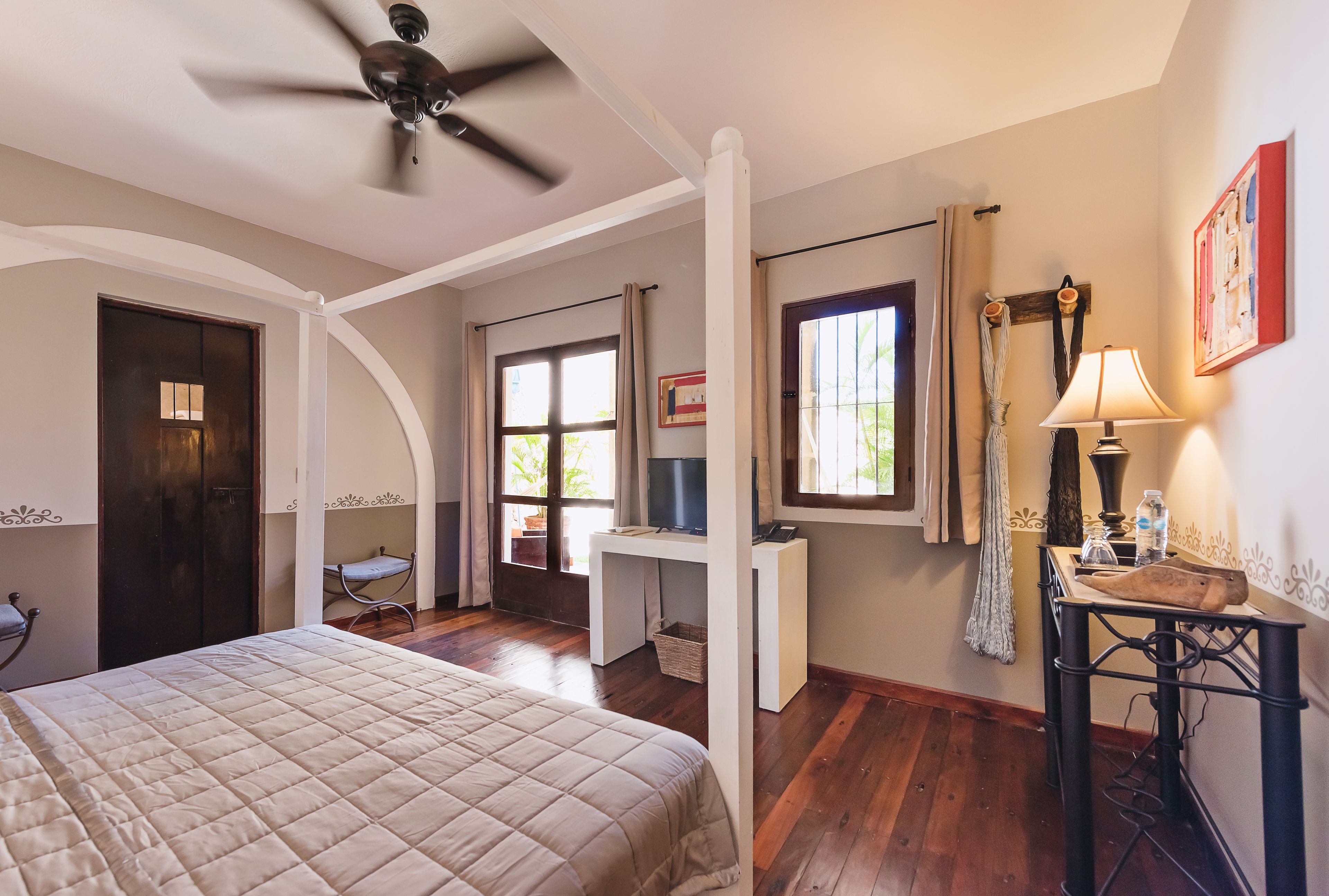 Un dormitorio con cama, escritorio, silla, ventilador de techo y ventana con cortinas.