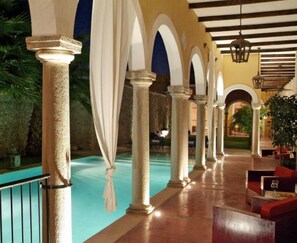 A hotel corridor with columns, a pool, and seating areas.