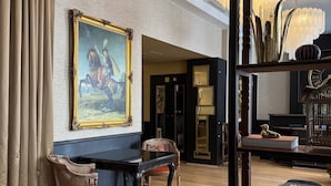 A room with a large painting, a piano, a bookshelf, and a chair. - New Hotel République (Paris)