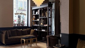 A living room with a sofa, a chair, a small table, a bookshelf, and a chandelier. - New Hotel République (Paris)