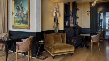 Une pièce comprenant un grand tableau encadré, un canapé, deux fauteuils, une petite table ornée d’objets décoratifs et une lampe.