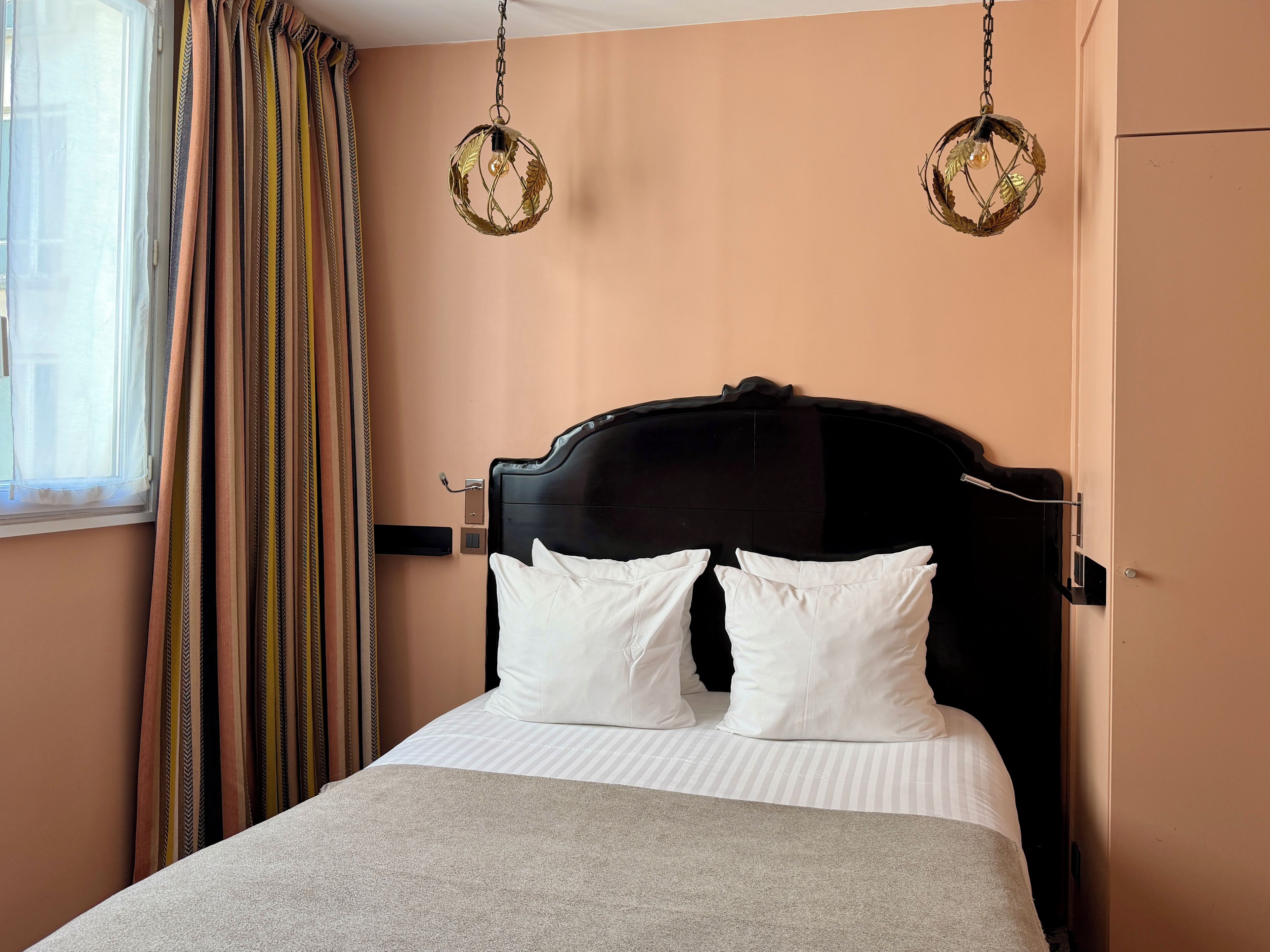 Una habitación de hotel con cama, cortinas y dos lámparas fijadas a la pared.