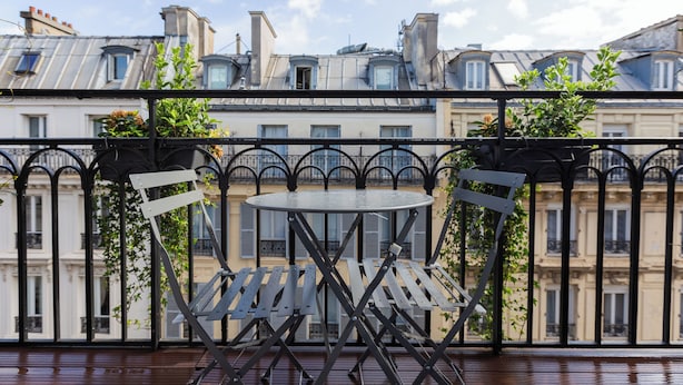 A balcony with a round table and two chairs, overlooking a row of buildings with balconies. - New Hotel République (Paris)
