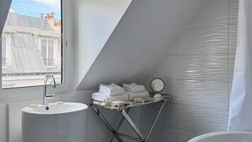 Une salle de bain moderne dotée d’un puits de lumière, d’un lavabo, d’une baignoire et d’un étendoir à linge avec des serviettes.