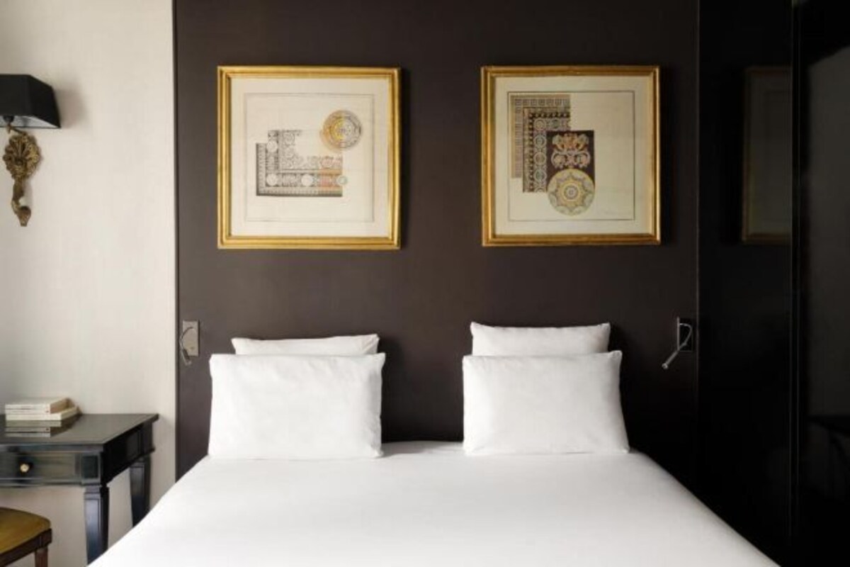 A hotel room with a bed, two framed artworks on the wall, a nightstand, and a lamp.