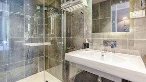 A modern bathroom with a glass-enclosed shower, a white sink, and a mirror with a wall-mounted light. - New Hotel République (Paris)