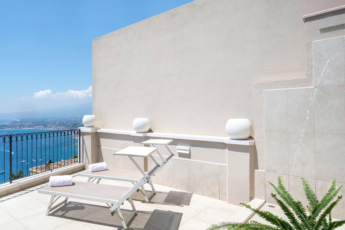 Een balkon met uitzicht op zee, een witte deur en een klein tafeltje met een stoel.