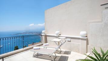 A balcony with a view of the sea, a white door, and a small table with a chair.