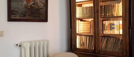 Una habitación con una estantería de madera llena de libros, un cuadro enmarcado de un velero y un tablero de ajedrez sobre una mesa.