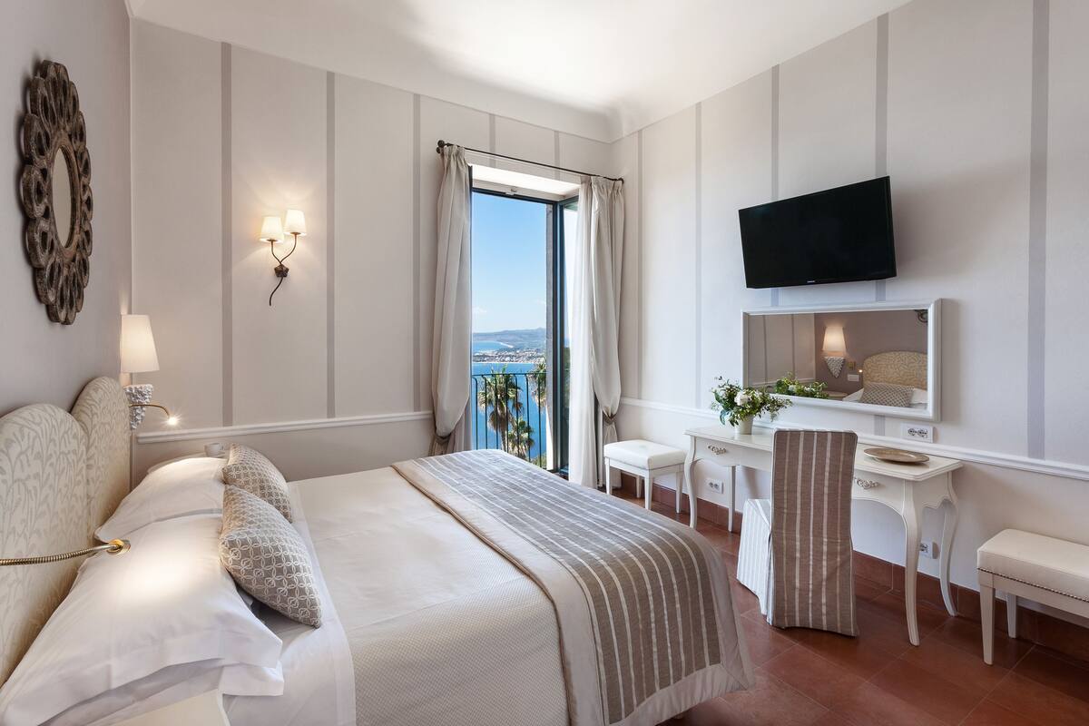 Een hotelkamer met een bed, een bureau, een stoel, een televisie en uitzicht over de stad.