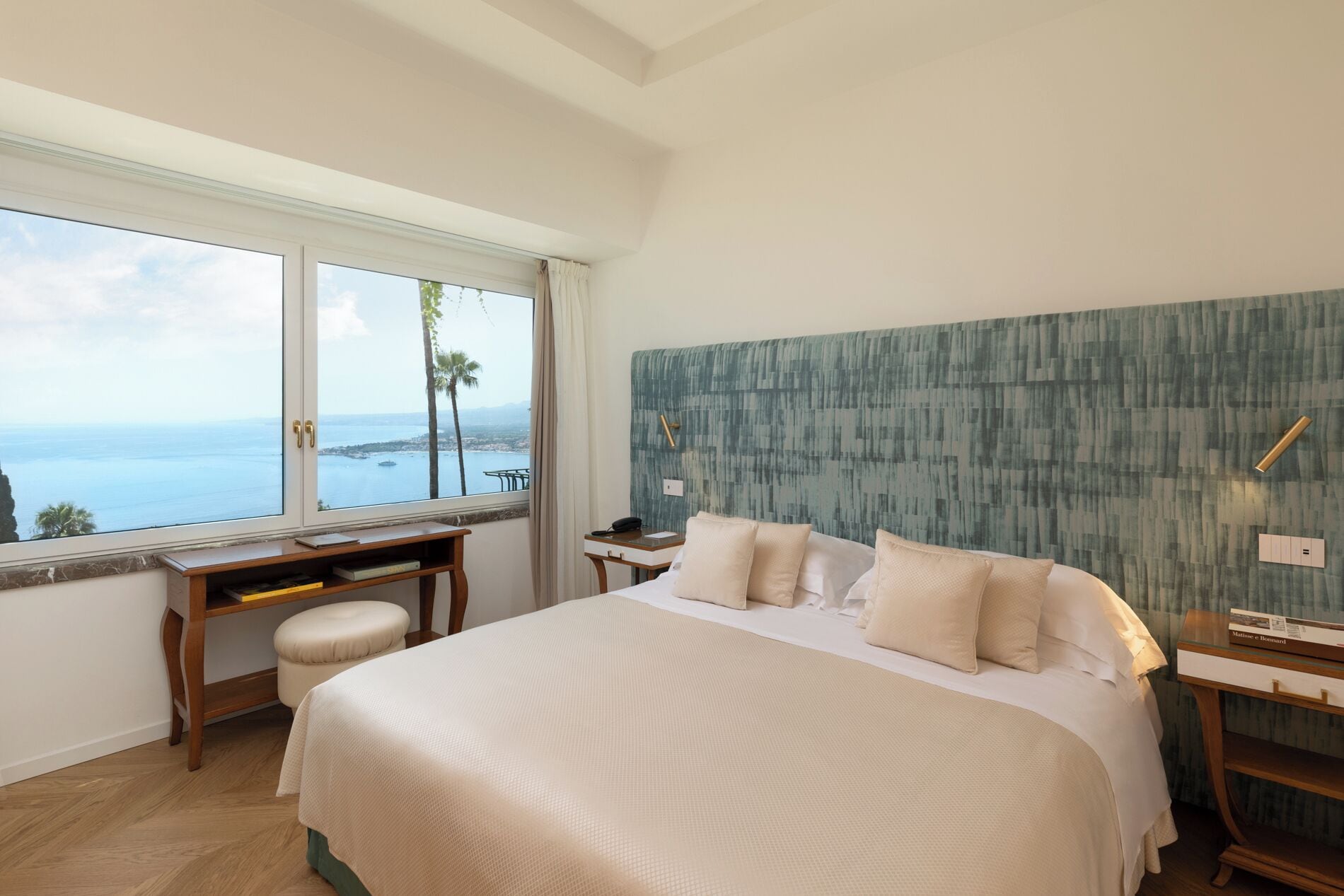 Une chambre avec un grand lit, un bureau et une vue sur la mer.